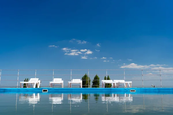 Tumbonas en el cielo azul de pie cerca de la piscina y se reflejan en el agua —  Fotos de Stock