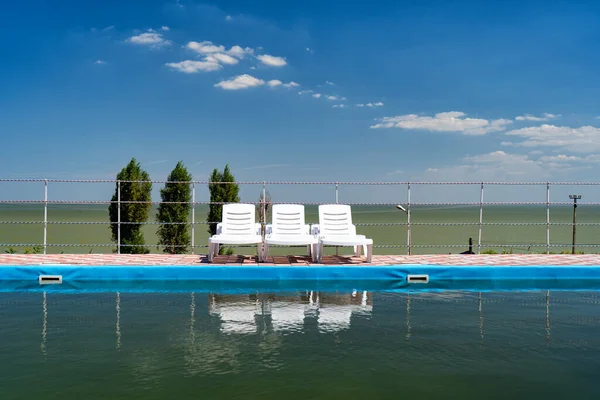 Tumbonas en el cielo azul de pie cerca de la piscina y se reflejan en el agua —  Fotos de Stock