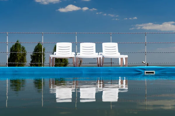 Tumbonas en el cielo azul de pie cerca de la piscina y se reflejan en el agua —  Fotos de Stock