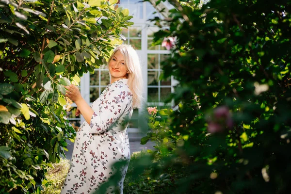 pregnant blonde in white dress in summer garden.