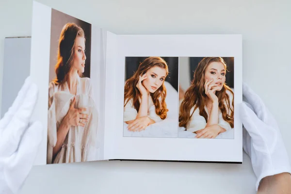 Manos en guantes blancos hojeando un libro de fotos con fotos de boda. — Foto de Stock