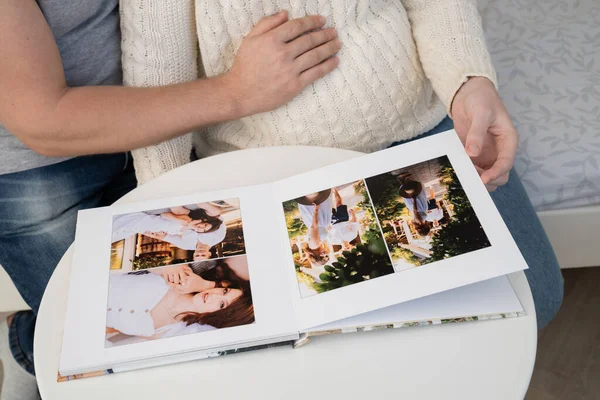 Casal à espera de bebê vira através do livro de fotos da sessão de fotos da família. — Fotografia de Stock
