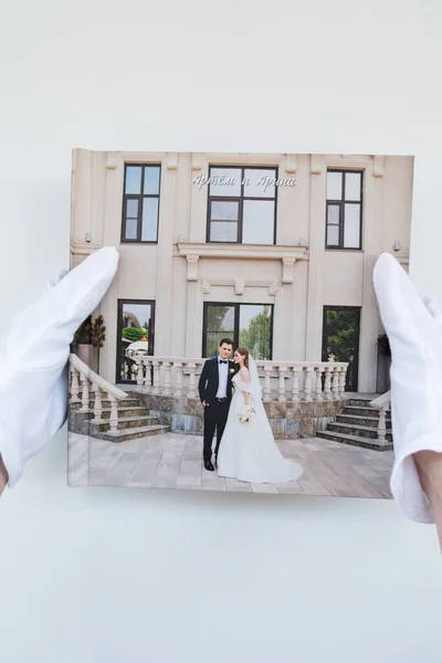 Mãos em luvas brancas segurando um livro de fotos com fotos de casamento. — Fotografia de Stock