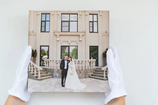 Mãos em luvas brancas segurando um livro de fotos com fotos de casamento. — Fotografia de Stock