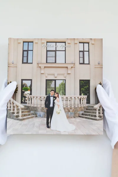 Mãos em luvas brancas segurando um livro de fotos com fotos de casamento. — Fotografia de Stock
