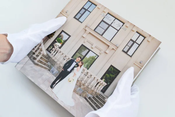 Mãos em luvas brancas segurando um livro de fotos com fotos de casamento. — Fotografia de Stock