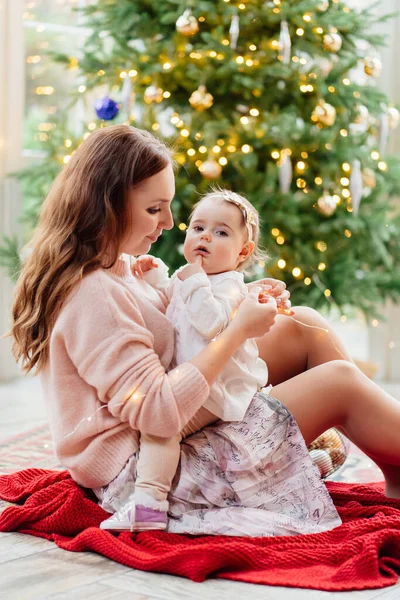 Madre e hija sentadas en el árbol de Navidad. — Foto de Stock