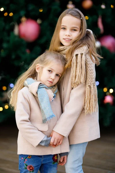 Małe dziewczynki w płaszczach w pobliżu dużej choinki — Zdjęcie stockowe