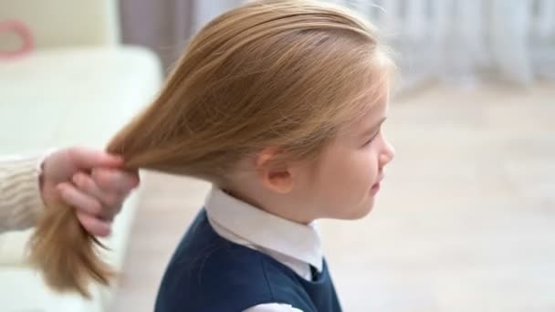 Vista lateral. chica de la escuela bosteza mientras que la madre peina el cabello. madrugada a la escuela. — Vídeos de Stock
