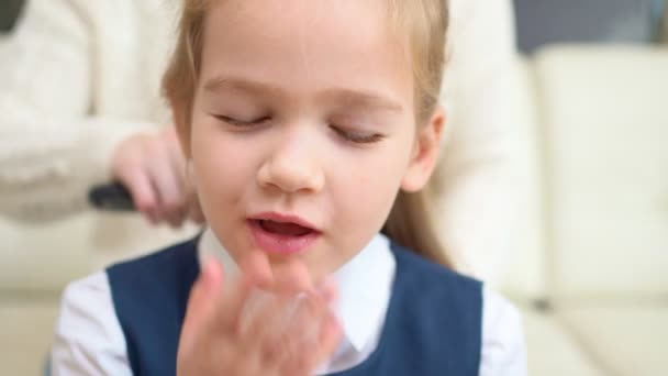 Ein süßes Schulmädchen gähnt, während Mutter die Haare kämmt. Frühe Einschulung. — Stockvideo