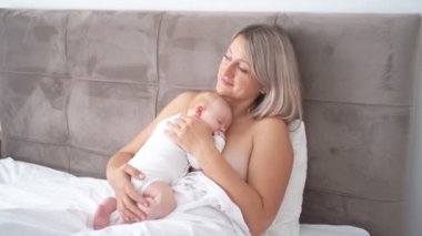 Çıplak anne, anne sütüyle beslendikten sonra uykulu bebekle oturuyor..
