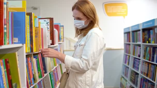 Koruyucu tıbbi maskeli bir kadın bir kitaptan ya da kütüphaneden kitap seçer. Rostov. - Rusya. 29 / 09 / 2020 — Stok video