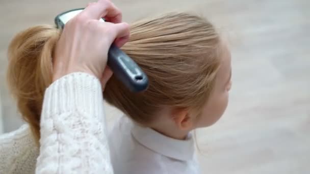 Gadis sekolah yang manis duduk sementara ibu menyisir rambut dan mengumpulkan ekor — Stok Video