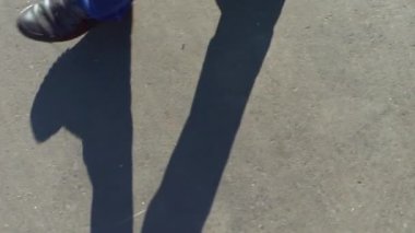 Bir adam bir asfalt yolda yürür. Kot pantolon ve karanlık çizmeler üstten görünüm bacaklar. Yaz güneşli gün ve bacaklar uzun bir gölge.