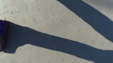 Bir adam bir asfalt yolda yürür. Kot pantolon ve karanlık çizmeler üstten görünüm bacaklar. Yaz güneşli gün ve bacaklar uzun bir gölge.