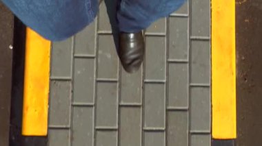 Bir adam bir kaldırım taşı kaldırım taşları içinde siyah ve sarı ile yürür. Kot pantolon ve karanlık çizmeler üstten görünüm bacaklar. Yaz güneşli gün.