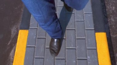Bir adam bir kaldırım taşı kaldırım taşları içinde siyah ve sarı ile yürür. Kot pantolon ve karanlık çizmeler üstten görünüm bacaklar. Yaz güneşli gün.