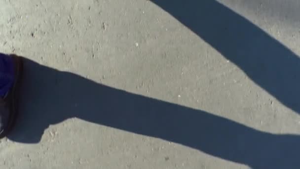 一个人走在沥青路面上 牛仔长裤双腿 黑靴顶部景观 夏日阳光明媚 腿部长满影子 — 图库视频影像