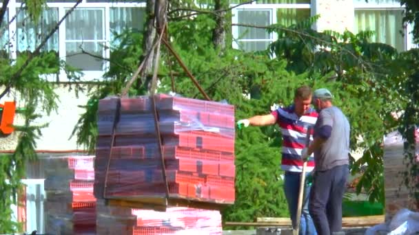 使用起重机和工人在建筑工地上卸砖 在阳光明媚的夏日 建筑材料的装配工作 — 图库视频影像