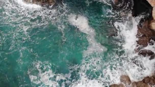 Flygfoto över vågorna bryter på stenar i ett blått hav. Havsvågor på vacker strand antenn utsikt drönare 4k skott. Fåglar syn på havet vågor kraschar mot en tom sten klippa uppifrån. — Stockvideo