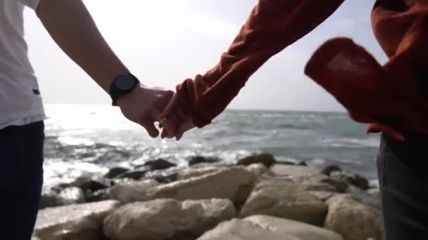 Archivvideo Nahaufnahme eines älteren kaukasischen Paares, das am Strand mit blauem Himmel und Meer im Hintergrund spaziert und sich in Zeitlupe an den Händen hält — Stockvideo