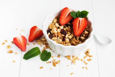 Granola ve beyaz ahşap bir masa üzerinde taze çilek ile kase
