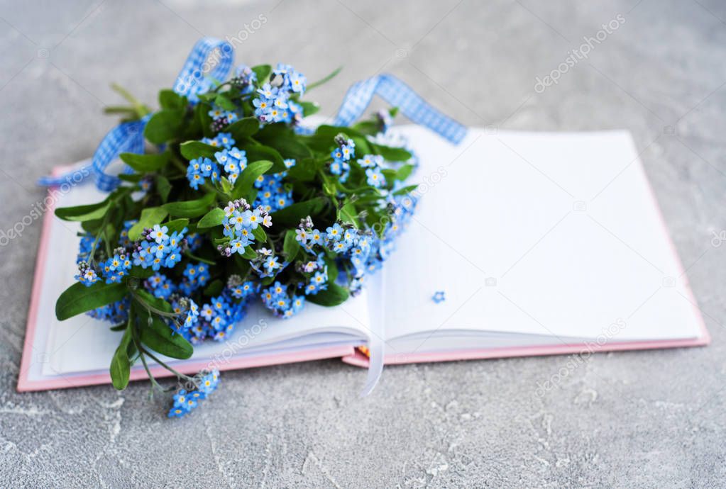 Forget me not flowers and notebook on grey stone background