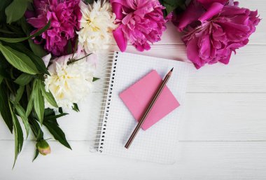 Beyaz ahşap zemin üzerinde peonies not defteriyle