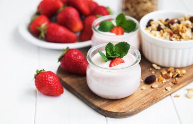 Sağlıklı Kahvaltı, yoğurt, taze çilek ve granola Beyaz ahşap bir masa üzerinde