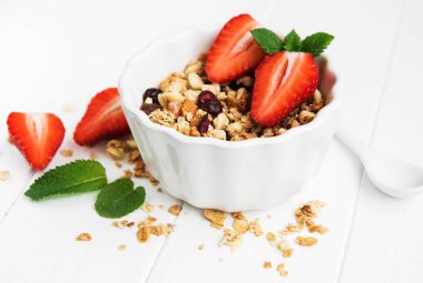 Granola ve beyaz ahşap bir masa üzerinde taze çilek ile kase
