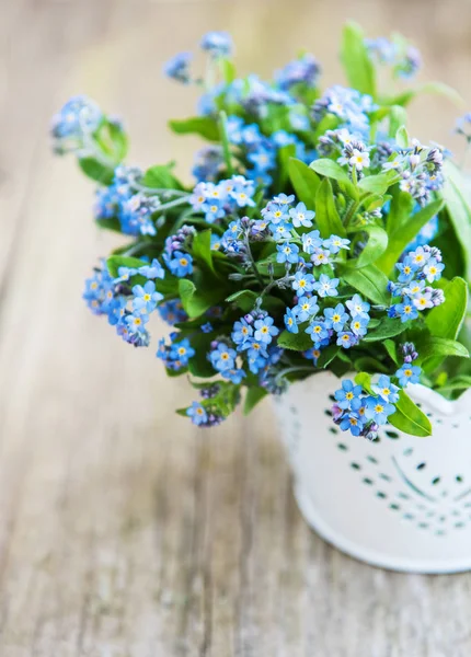 Forget-me-not flowers in small metal bucket on old table