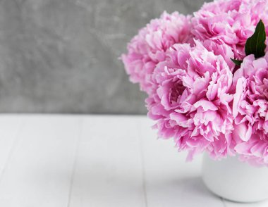 Beyaz ahşap bir masa üzerinde pembe şakayık çiçekli vazo