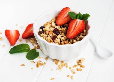Granola ve beyaz ahşap bir masa üzerinde taze çilek ile kase