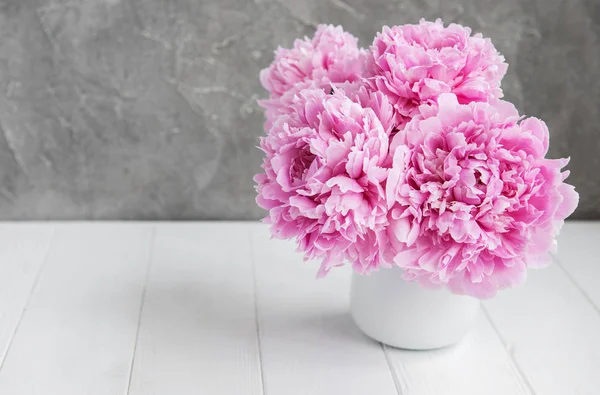 Beyaz ahşap bir masa üzerinde pembe şakayık çiçekli vazo