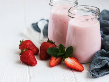Kavanoz bir beyaz tahta masada çilekli yoğurt ile