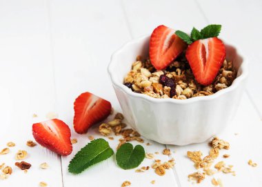 Granola ve beyaz ahşap bir masa üzerinde taze çilek ile kase