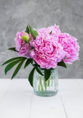 Beyaz ahşap bir masa üzerinde pembe şakayık çiçekli vazo