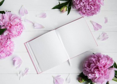 Beyaz ahşap zemin üzerinde peonies not defteriyle