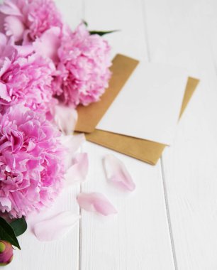 davetiye, zanaat zarf ve pembe şakayık çiçekleri Beyaz ahşap bir masa üzerinde
