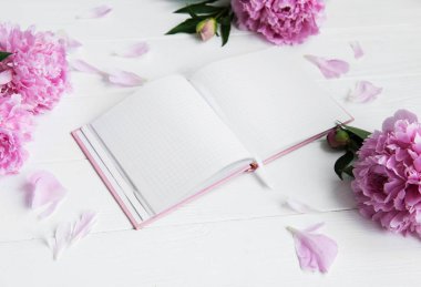 Beyaz ahşap zemin üzerinde peonies not defteriyle