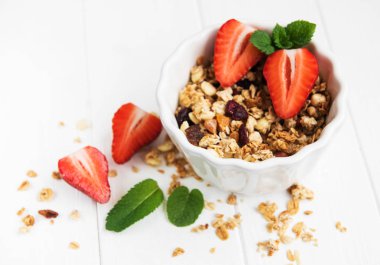 Granola ve beyaz ahşap bir masa üzerinde taze çilek ile kase