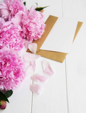 davetiye, zanaat zarf ve pembe şakayık çiçekleri Beyaz ahşap bir masa üzerinde