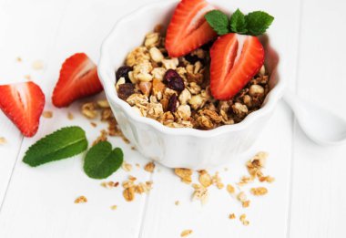 Granola ve beyaz ahşap bir masa üzerinde taze çilek ile kase