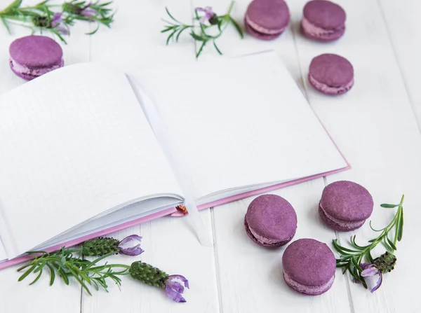 French macaroons, clean notebook and lavender flowers on a white wooden background