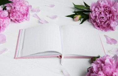 Beyaz ahşap zemin üzerinde peonies not defteriyle