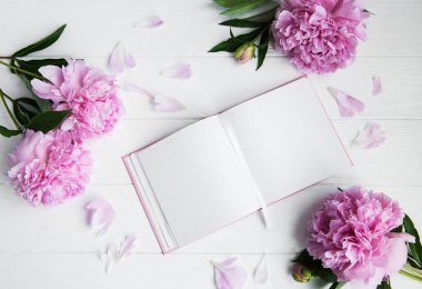 Beyaz ahşap zemin üzerinde peonies not defteriyle