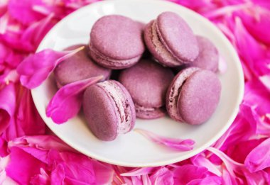 Beyaz ahşap bir masa üzerinde macarons ile pembe şakayık yaprakları
