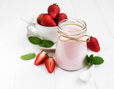 Beyaz ahşap bir masa üzerinde çilekli yoğurt ile jar