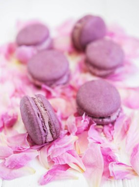Beyaz ahşap bir masa üzerinde macarons ile pembe şakayık yaprakları