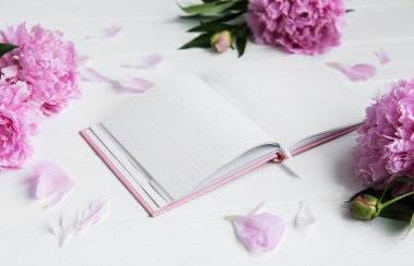Beyaz ahşap zemin üzerinde peonies not defteriyle
